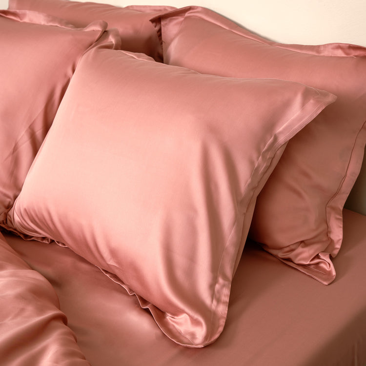 Vier terra roze kussenslopen van de stof Tencel op een bed 
